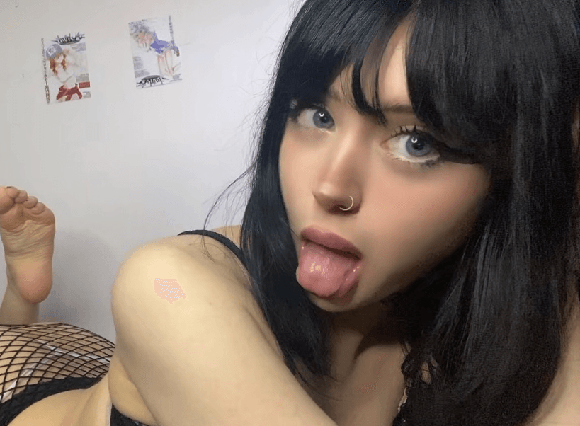 Close-up portrait of a young woman with black hair and a nose ring, sticking out her tongue toward the camera.