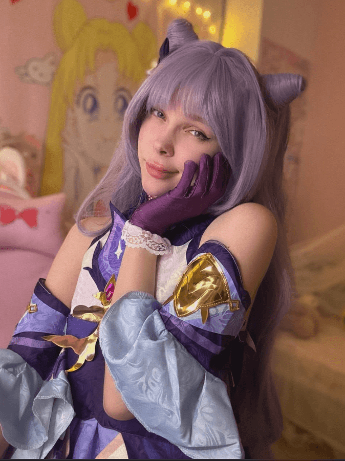Cosplayer in a purple-lavender costume with cat ears, posing with chin resting on gloved hand in a pastel bedroom.