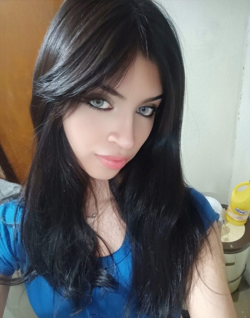 Close-up portrait of a woman with long dark hair and a blue top, looking at the camera with a neutral expression.